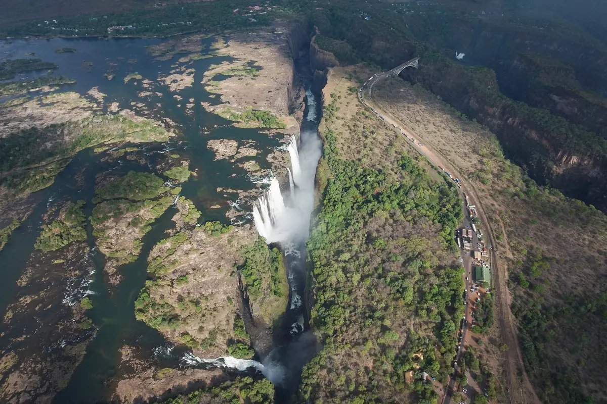 An aerial view of Victoria Falls dropping into a narrow gorge, with the bridge arching across the top right (a daytime view of the falls, not of the theatre)