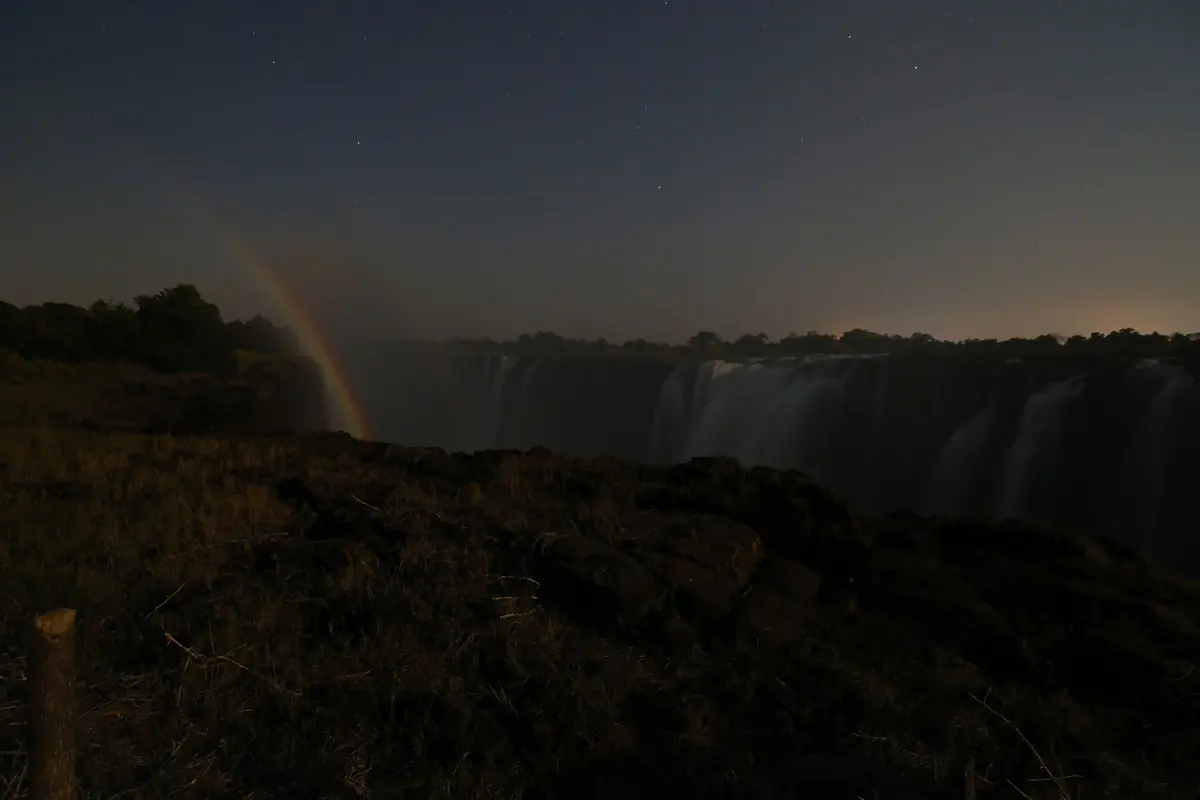 A faint lunar rainbow rising beside the falls at night under a starry sky (the falls after dark, not the theatre)